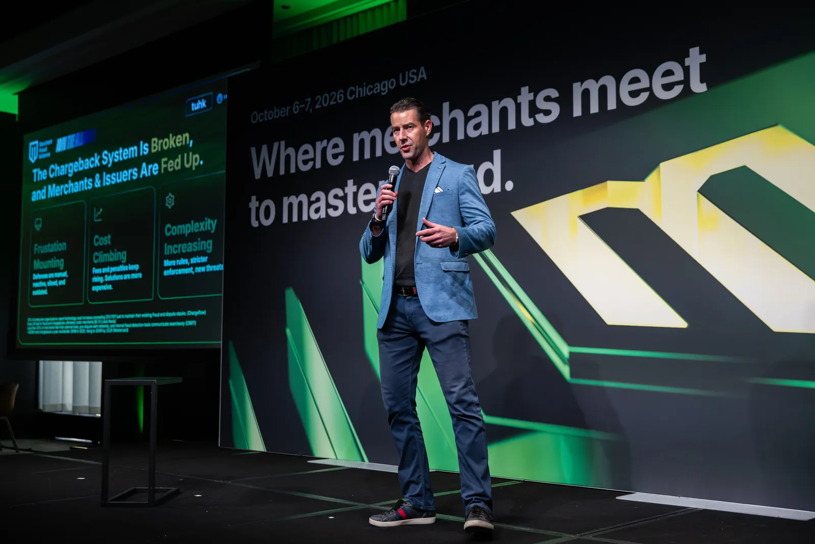 A speaker on stage in front of the green key visual and a slide on the chargeback system