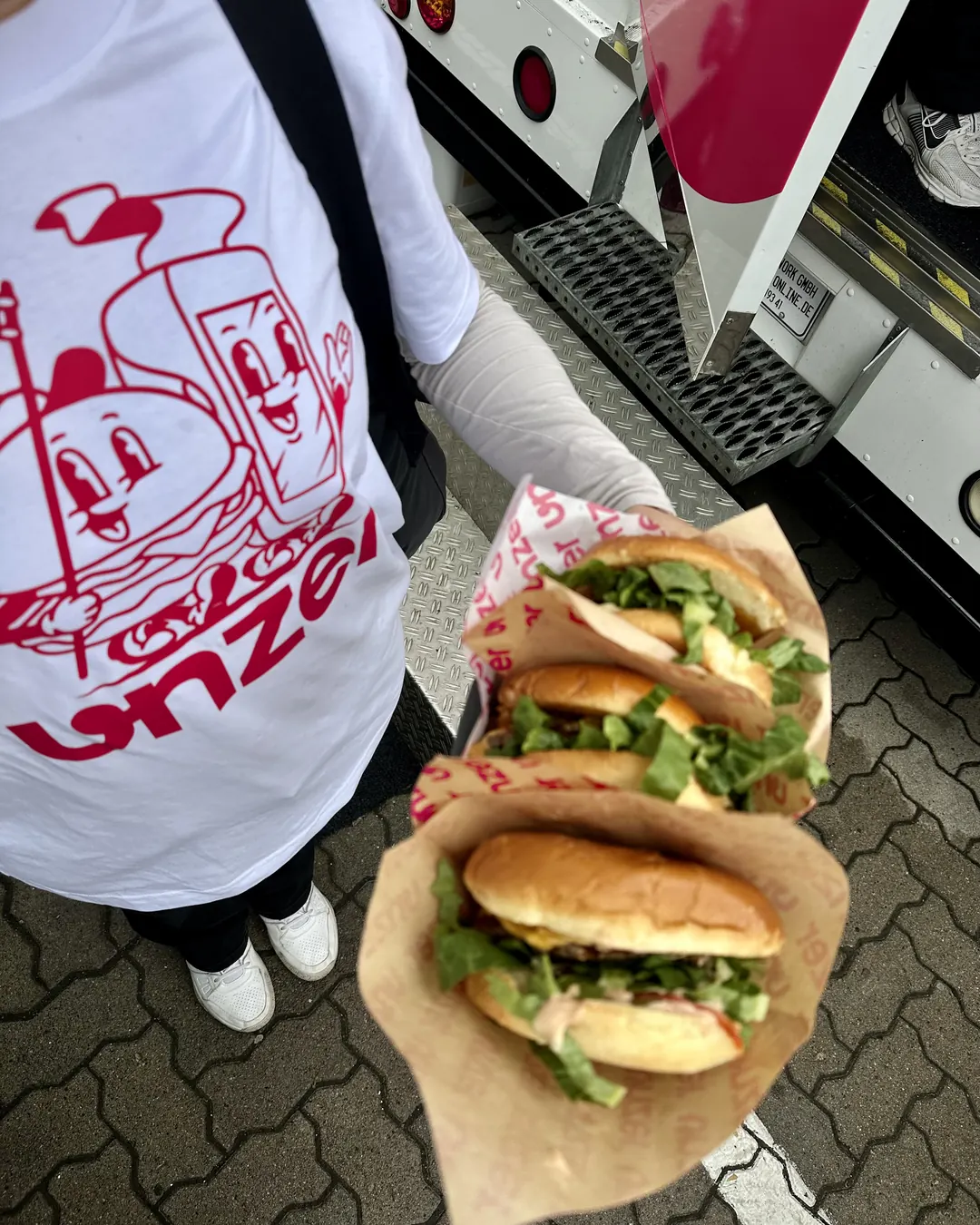 Three burgers in Unzer wraps held in front of the truck by a guest in the mascot shirt