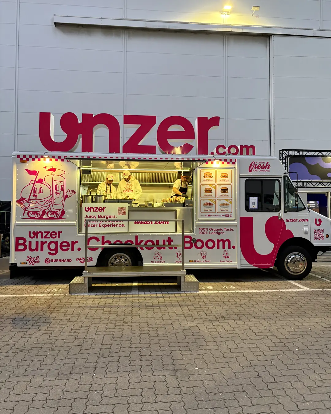 The Unzer food truck lit up in the evening in front of a hall at the fair