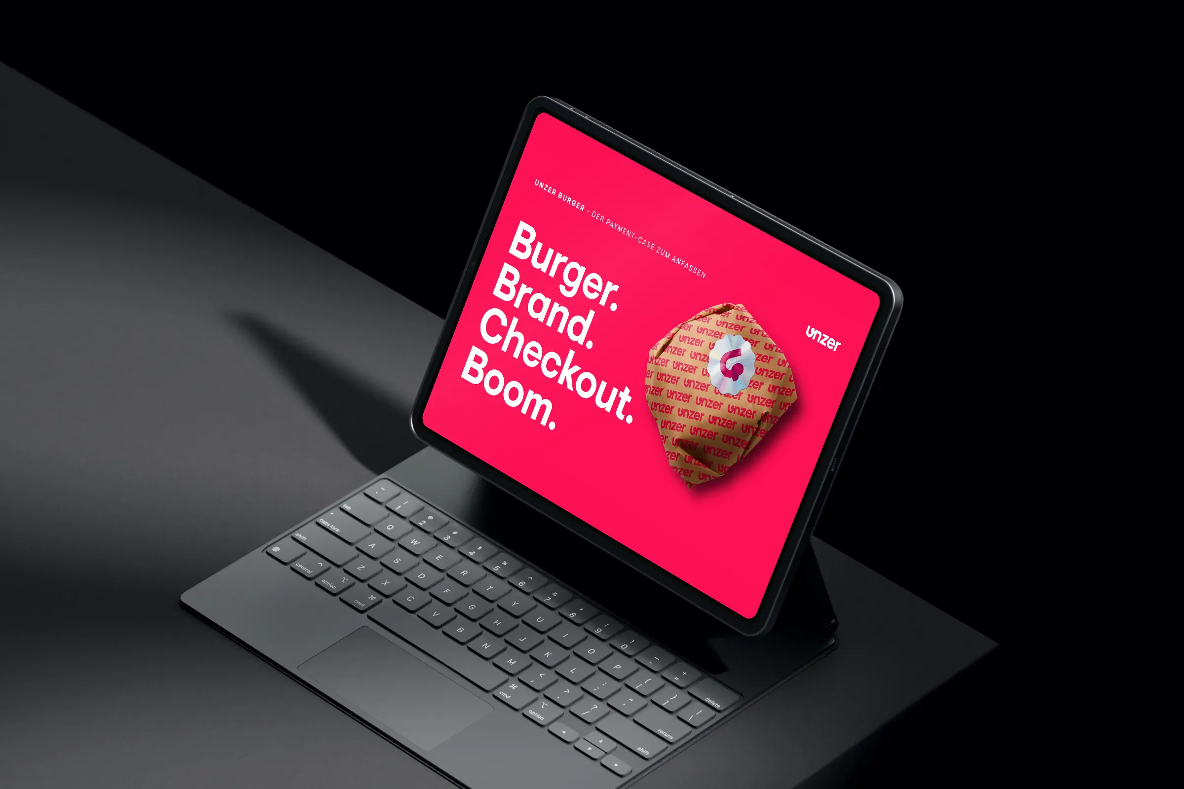 Tablet with keyboard on a dark table showing the pitch deck cover “Burger. Brand. Checkout. Boom.” with a burger in an Unzer wrap