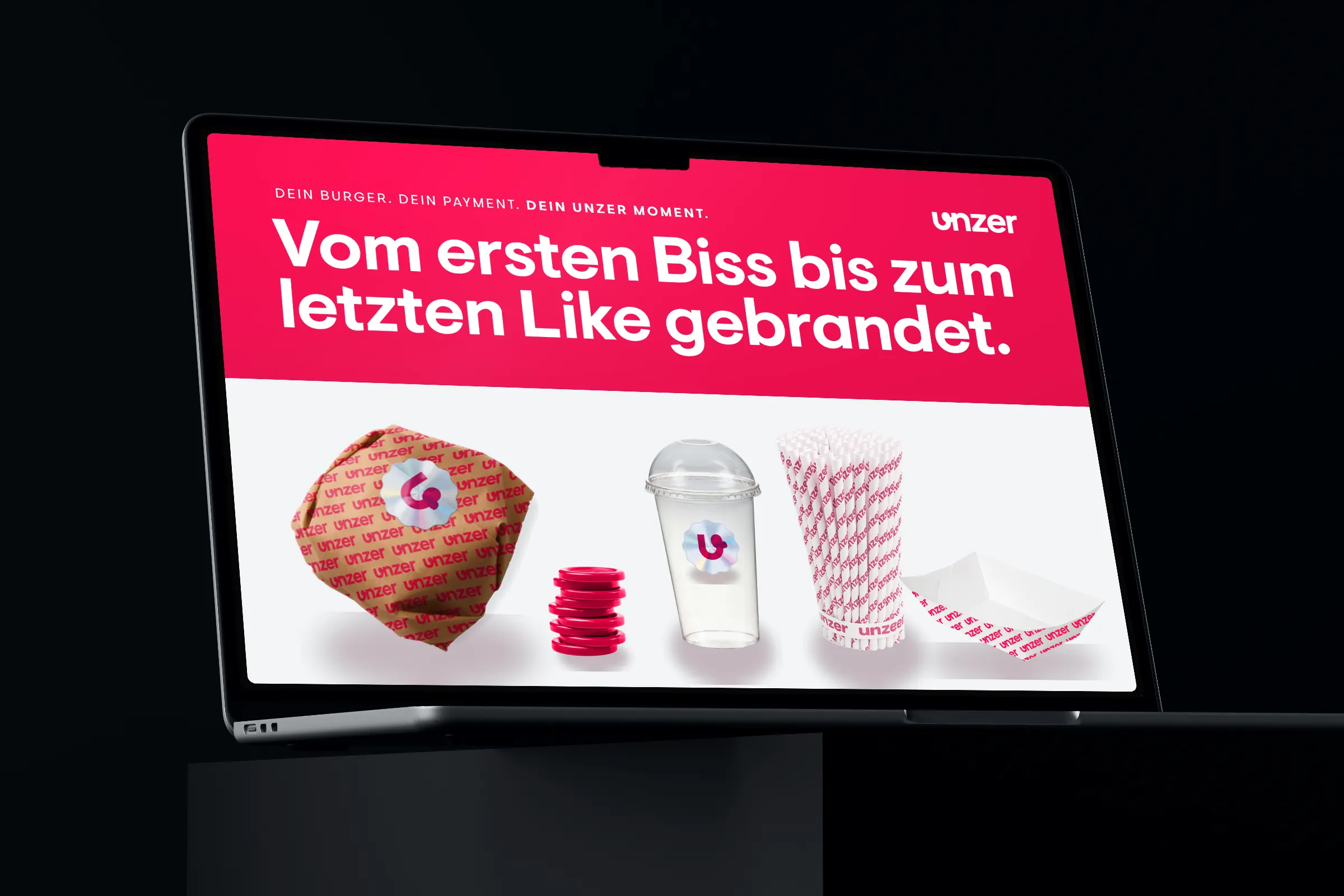 Laptop on a dark plinth showing the pitch slide with burger wraps, cups, fries trays and voucher chips in the Unzer look